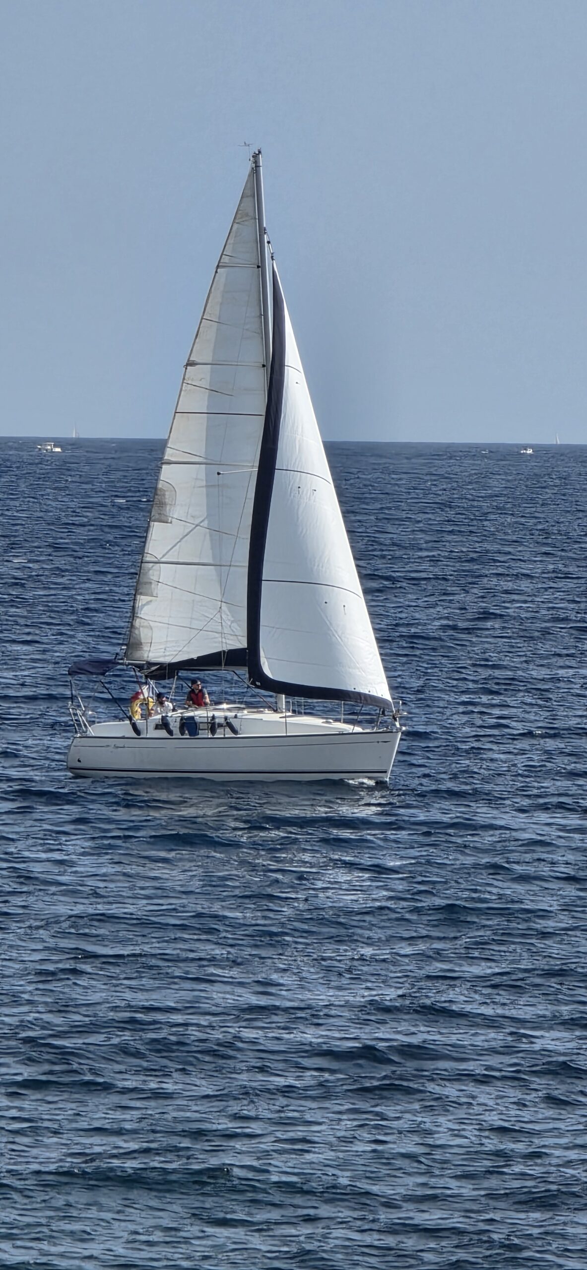 Voilier aux voiles blanches naviguant sur une mer bleue.